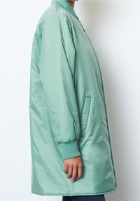 Lehká polstrovaná bunda světle zelené barvy s žebrovanými manžetami a límcem, zapínáním na zip a bočními kapsami. Hladká, lesklá textura látky.