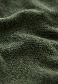 Dunkelgrüner Strickstoff mit einer weichen Textur, der ein dezentes, meliertes Muster aufweist. Die Oberfläche wirkt leicht locker und geschmeidig.