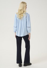 Gaiši zila blūze ar savelktām plecu daļām un acu caurumiem uz piedurknēm, pārī ar tumšām platām džinsiem un melniem masīvajiem apaviem.