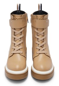 Botas de cuero beige con un diseño de cordones, cremallera lateral, suela media blanca y un puño texturizado. Presentan una lengua de agarre con franjas negras y beige.