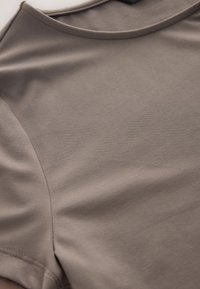 Lysebrun top med korte ærmer lavet af blødt stof, der har en glat tekstur og en rund halsudskæring med diskrete syningsdetaljer.