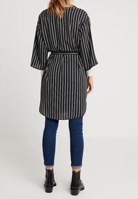 Zwart-wit gestreepte lange kimono met brede mouwen, ceintuur in de taille, gecombineerd met strakke blauwe jeans en enkellaarsjes.