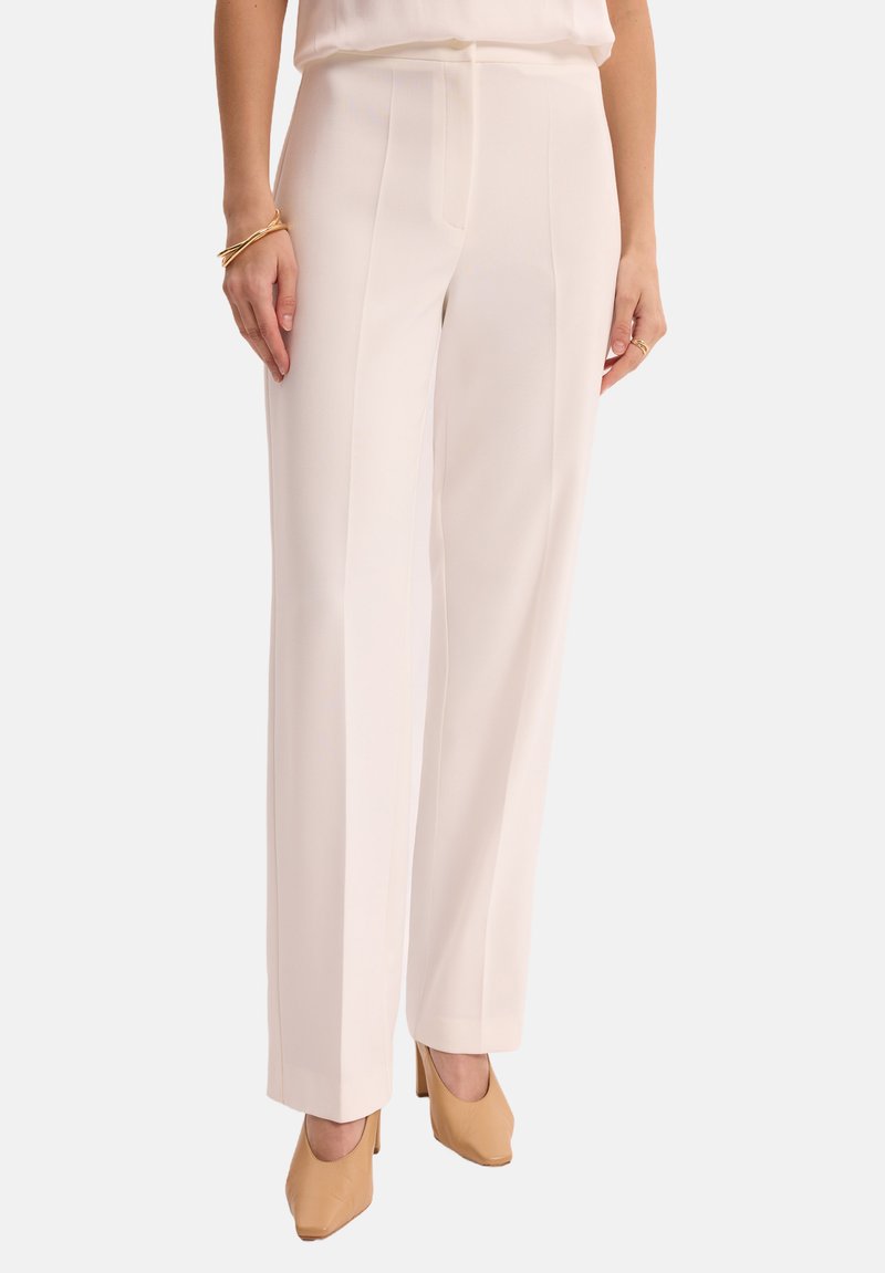Szerokie spodnie w miękkim, jasnokremowym materiale. Charakteryzują się gładką fakturą, przednimi zmarszczeniami i luźnym krojem. W połączeniu z beżowymi szpilkami.
