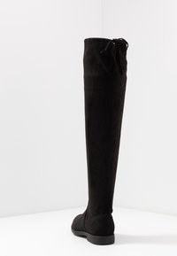 Bota negra por encima de la rodilla hecha de suave ante, con suela plana y un detalle de lazo en la parte superior para un ajuste ajustable.
