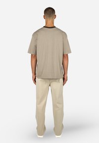 Szara bawełniana koszulka z brązowym ozdobnym dekoltem, w połączeniu z beżowymi spodniami o luźnym kroju. Materiał jest gładki z luźnym fasonem.