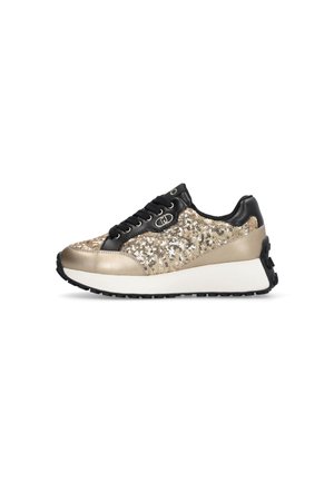 Chaussure de sport lacée en noir et or. Elle présente un dessus en paillettes, des accents métalliques, un col rembourré et une épaisse semelle blanche avec un dessous noir.