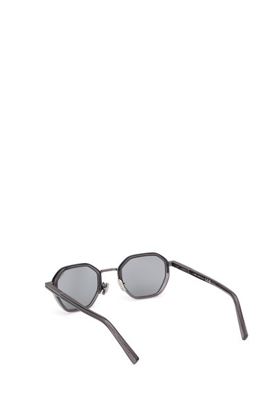 Ochelari de soare octagonali cu lentile gri închis, rame subțiri negre, temple texturate și un accent metalic pe balamale.