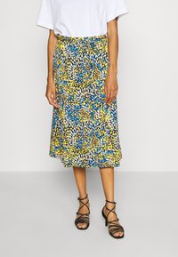 Falda floral en azul, amarillo y blanco con cintura ajustada, diseño fluido y dobladillo a nivel del tobillo. Combinada con tacones negros con tiras.