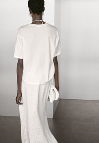 Weißes Baumwoll-T-Shirt mit entspannter Passform, kurzen Ärmeln und einem Detail mit Bindeband am Rücken, kombiniert mit einem langen, strukturierten, weißen Strickrock.