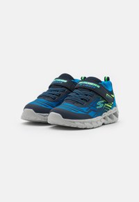 Baskets de sport bleu marine avec des accents bleu clair et vert, tige texturée, sangle ajustable et semelle en caoutchouc grise avec un motif de semelle.