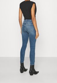 Höga blå denimjeans med smal passform, slitna detaljer och två bakfickor, kombinerade med svarta ankelofflor.