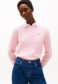 Pull en tricot rose clair avec un motif texturé, doté d'un col rond. Associé à un jean en denim bleu foncé taille haute.