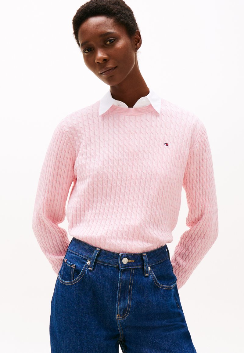Pull en tricot rose clair avec un motif texturé, doté d'un col rond. Associé à un jean en denim bleu foncé taille haute.