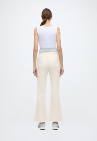 Haut blanc sans manches associé à un pantalon évasé crème taille haute. Le pantalon présente une texture douce et est agrémenté d'accents gris.