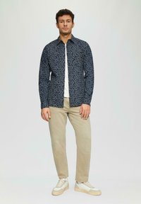 Koszula w marynarskim wzorze z białymi akcentami, z kołnierzykiem zapinanym na guziki, w połączeniu z jasnobeżowymi spodniami i kremowymi sneakersami. Slim fit.