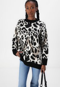 Suéter de gran tamaño con un diseño de estampado de leopardo, en colores negro, beige y blanco, con un cuello y un dobladillo de ribete negro.