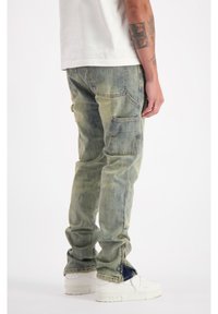 Cargo jeans in vervaagde lichtgroene denim, met meerdere zakken, een relaxte pasvorm en ritssluitingen bij de boorden. Gecombineerd met witte sneakers.