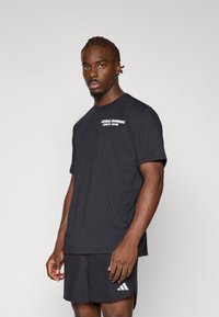 Černé tričko s krátkým rukávem vyrobené z bavlny, s bílým textem "ADIDAS RUNNING SINCE 1949" na levé části hrudi. Jednoduchý, uvolněný střih.