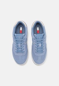 Sneakers scamosciati azzurro chiaro con suole in gomma bianca, caratterizzati da un design con lacci, cuciture sottili e un'etichetta con logo all'interno.