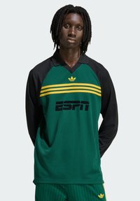 Zelena sportska majica s dugim rukavima, crnim rukavima, žutim prugama i logotipom ESPN-a. Ima ovratnik i tkaninu s teksturom.