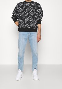 Černá mikina s bílým grafickým textem, spárovaná se světle modrými džíny a bílými teniskami. Mikina má žebrované manžety a lem.