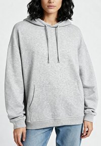 Szara bluza z kapturem, z kieszenią na przodzie, ściągaczami przy mankietach i u dołu. Wykonana z miękkiego materiału, posiada luźny krój i kaptur ze sznurkiem.
