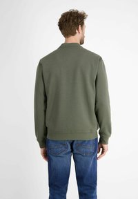 Olive green sweatshirt with a crew neck, ribbed cuffs, and hem; styled with blue denim jeans. Smooth, soft fabric texture.