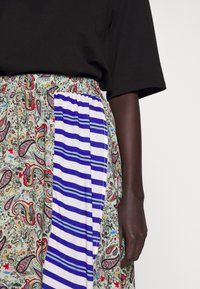 Maxi sukně s paisley potiskem v zelené, červené a modré barvě a bočním panelem modro-bílých pruhů. Elastický pas.