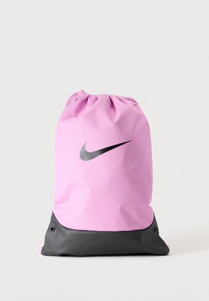 Sac de sport rose à cordon avec fond noir et logo Nike Swoosh noir à l'avant sur fond gris clair.