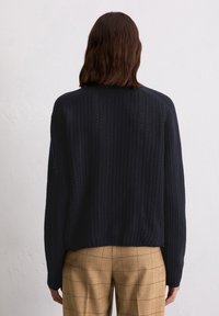 Marineblauer Strickpullover mit vertikal gerippter Textur, Rundhalsausschnitt und überschnittenen Schultern, kombiniert mit beigefarbenen Karohosen.