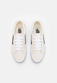Beige suede sneakers with white laces, black side stripes, and a perforated toe design. Features a rubber sole with black trim.