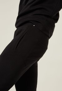 Zwarte joggingsbroek van zachte stof, met zijzakken, subtiele plooien en een aansluitend ontwerp. Eenvoudige en functionele stijl.