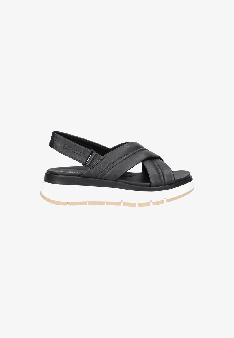 Sandales en cuir noir avec un design à lanières croisées, une sangle de talon ajustable, et une semelle en caoutchouc blanche et beige avec une texture antidérapante.