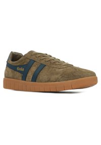 Bruine suède sneaker met donkerblauwe strepen en een rubberen zool. Kenmerkt zich door een ronde neus, platte veters en merkdetails aan de zijkant.