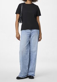 Svart kortärmad T-shirt, avslappnad passform, matchad med ljusblå vida jeans och svarta platåsandaler. Tillbehör inkluderar en liten svart väska.