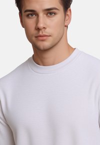Sweatshirt blanc avec un col rond et un tissu texturé. Présente une sensation douce et extensible ainsi qu'une coupe ajustée. Aucun motif ou accent visible.