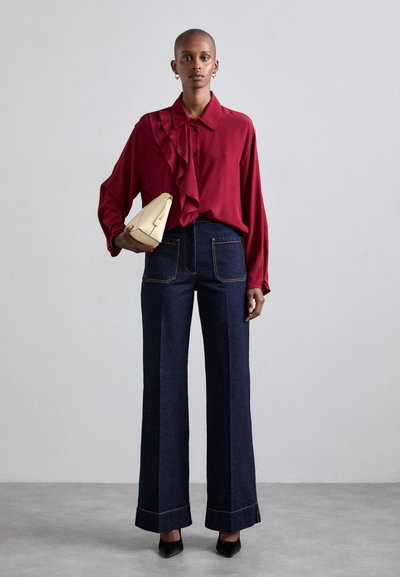 Κόκκινη μπλούζα με φρου φρου, ψηλόμεσα σκούρα τζιν παντελόνια με κωδική γραμμή, και κρέμα τσαντάκι. Μαύρες μυτερές γόβες και ελάχιστα αξεσουάρ.