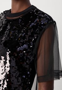 Haut noir à manches courtes avec des sequins noirs brillants sur le devant et des manches en tissu mesh transparent.
