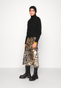 Veste en denim noir avec deux poches sur la poitrine, associée à une jupe satinée longueur genoux avec un motif zèbre noir et beige et des bottines noires.