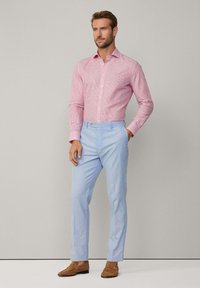 Czerwona i biała w paski koszula z guzikami, w połączeniu z jasnoniebieskimi spodniami w paski i brązowymi loafersami, wszystko na neutralnym tle.