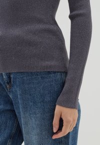 Dunkelgrauer, gerippter Strickpullover, figurbetontes Design, lange Ärmel mit breiten Bündchen, kombiniert mit hellblauen Denim-Jeans.