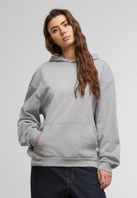 Felpa grigia con cappuccio e maniche lunghe, tasca frontale e orlo a coste. Tessuto morbido e vestibilità comoda. Abbinata a jeans scuri.