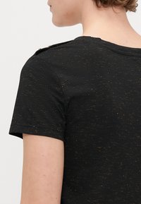 Sort t-shirt med korte ærmer og struktureret finish, med guldtråd detaljer og skulderknapper for ekstra detalje og design.