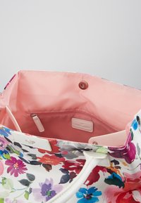 Tkaná taška s květinovým vzorem a bílými koženými detaily, otevřená s růžovým interiérem. Obsahuje zipovou kapsu a značkovou nálepku.