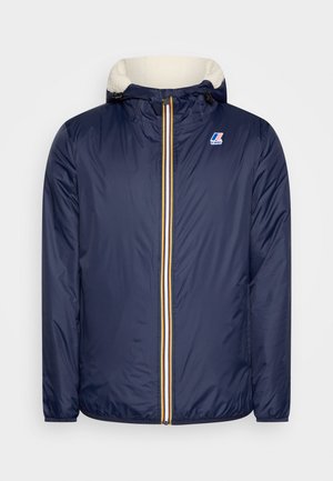 Giacca puffer blu navy con chiusura a zip, accenti a righe gialle e bianche e cappuccio foderato in pelliccia. Presenta polsini elastici e toppa con logo.