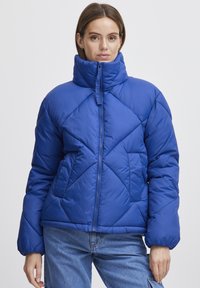 Blå puffjacka med hög krage, diamantformad quiltning, dragkedja fram och sidofickor. Tillverkad av mjukt, vadderat material.