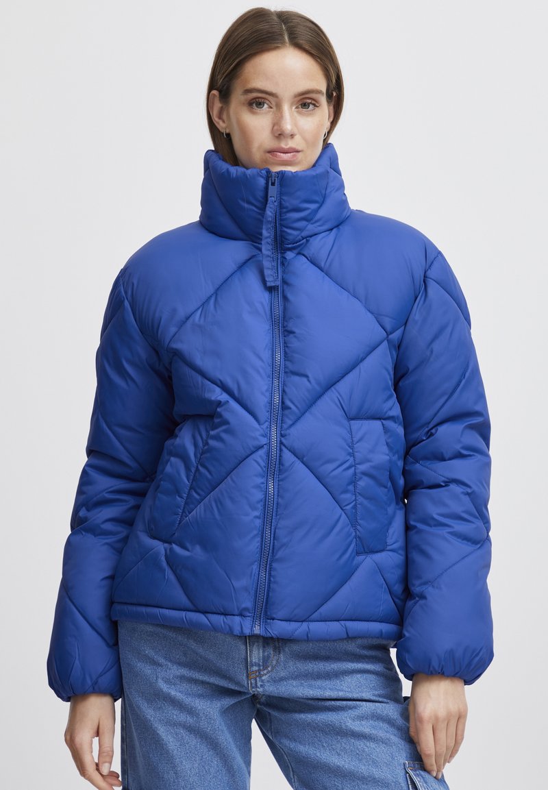 Blå puffjacka med hög krage, diamantformad quiltning, dragkedja fram och sidofickor. Tillverkad av mjukt, vadderat material.