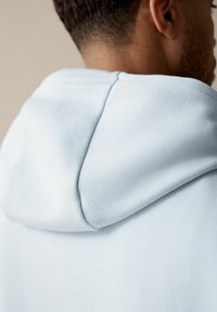 Helleblaues Kapuzensweatshirt mit weichem Stoff, abgerundeter Kapuze und sichtbaren Nahtdetails an Hals und Schultern.