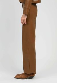 Pantalons taille haute en cuir marron, design à jambe droite, texture lisse, sans coutures visibles, portés avec des bottes de cow-boy marron brodées.