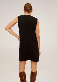 Robe noire sans manches avec un col haut, présentant une coupe droite, une texture lisse et une fermeture éclair dissimulée dans le dos.